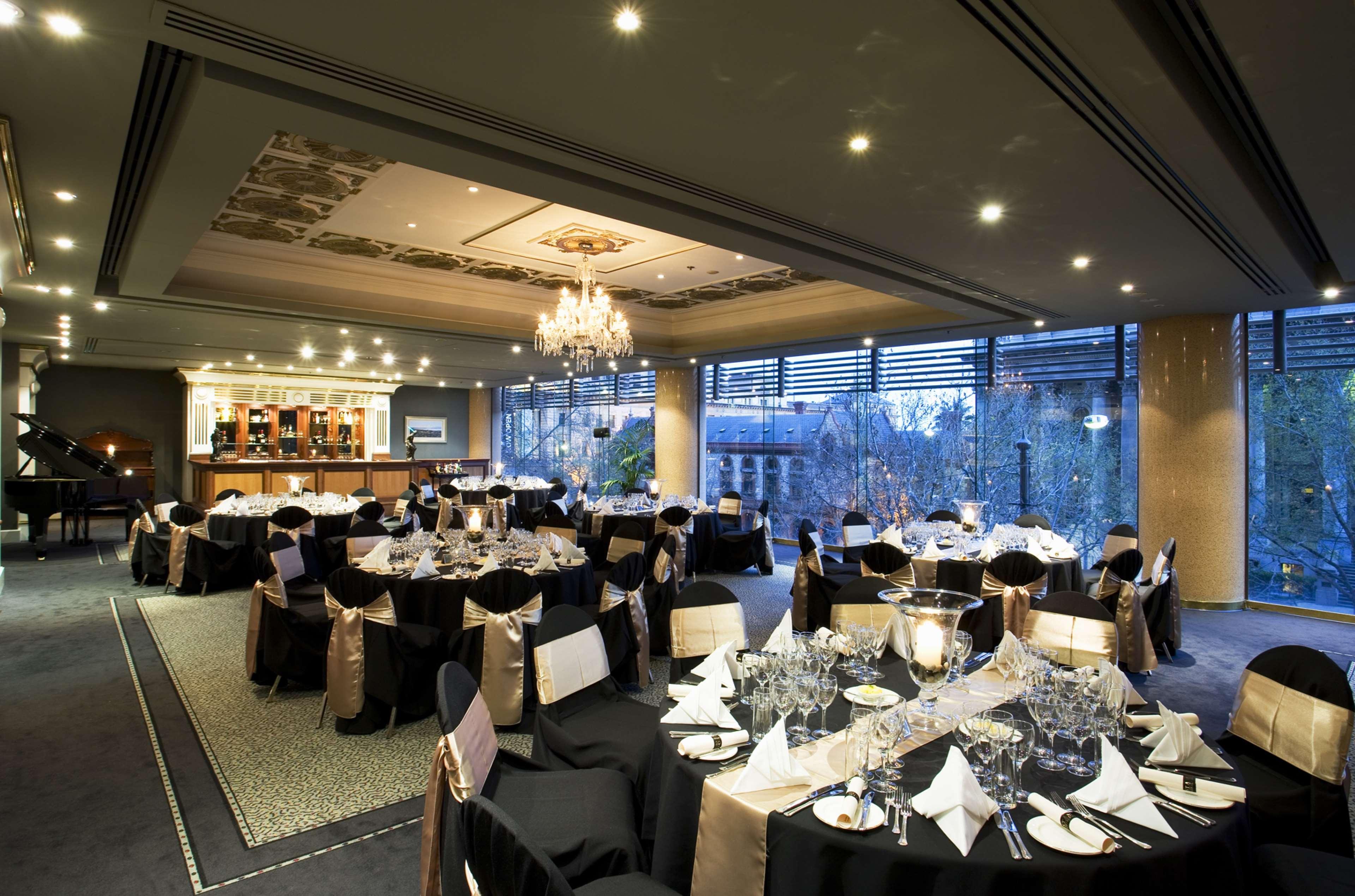 Hotel Stamford Plaza Adelaïde Extérieur photo The photo shows an elegant banquet hall or restaurant setting. There are several round tables covered with black tablecloths and adorned with gold accents. Each table is set with fine dining utensils, glassware, and neatly folded napkins. In the back