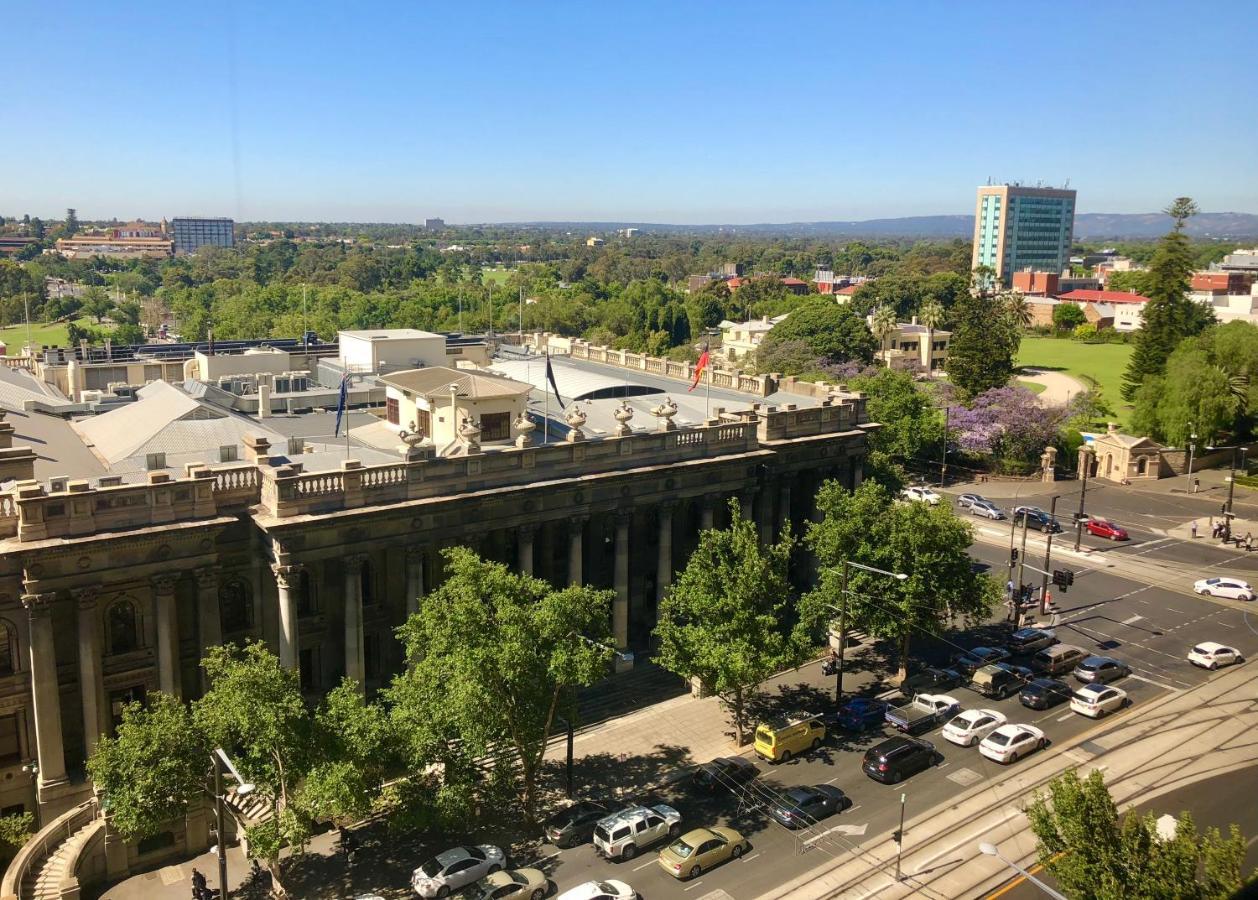 Hotel Stamford Plaza Adelaïde Extérieur photo The photo depicts a cityscape view, showcasing a mix of architectural structures and greenery. In the foreground, there is a large, classical building with columns, suggesting it may be a historical or governmental structure. Surrounding the building